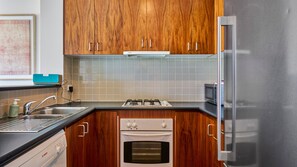 Una cocina con armarios de madera, estufa a gas, horno, microondas y refrigerador de acero inoxidable.