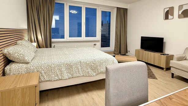 Une chambre d’hôtel moderne équipée d’un lit, d’une télévision, d’un bureau et d’une fenêtre avec des rideaux.