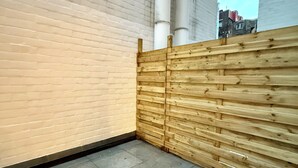 Un coin d’un bâtiment avec un sol carrelé, une clôture en bois et un mur en briques.