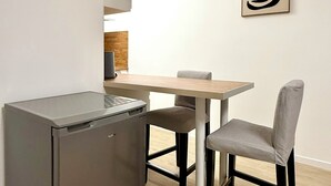 Une cuisine compacte dotée d’un réfrigérateur intégré, d’une table à manger avec deux chaises et d’une œuvre d’art murale au style minimaliste.