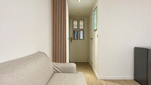 Un salon moderne avec un canapé, un mur recouvert de lambris en bois, une porte donnant sur une autre pièce et un petit meuble.