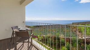 Un balcón con una mesa lista para dos personas, con vistas a un jardín y al mar.
