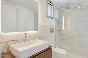 A modern bathroom with a large rectangular sink, a toilet, and a glass-enclosed shower area. - Isabel Place (Câmara de Lobos)