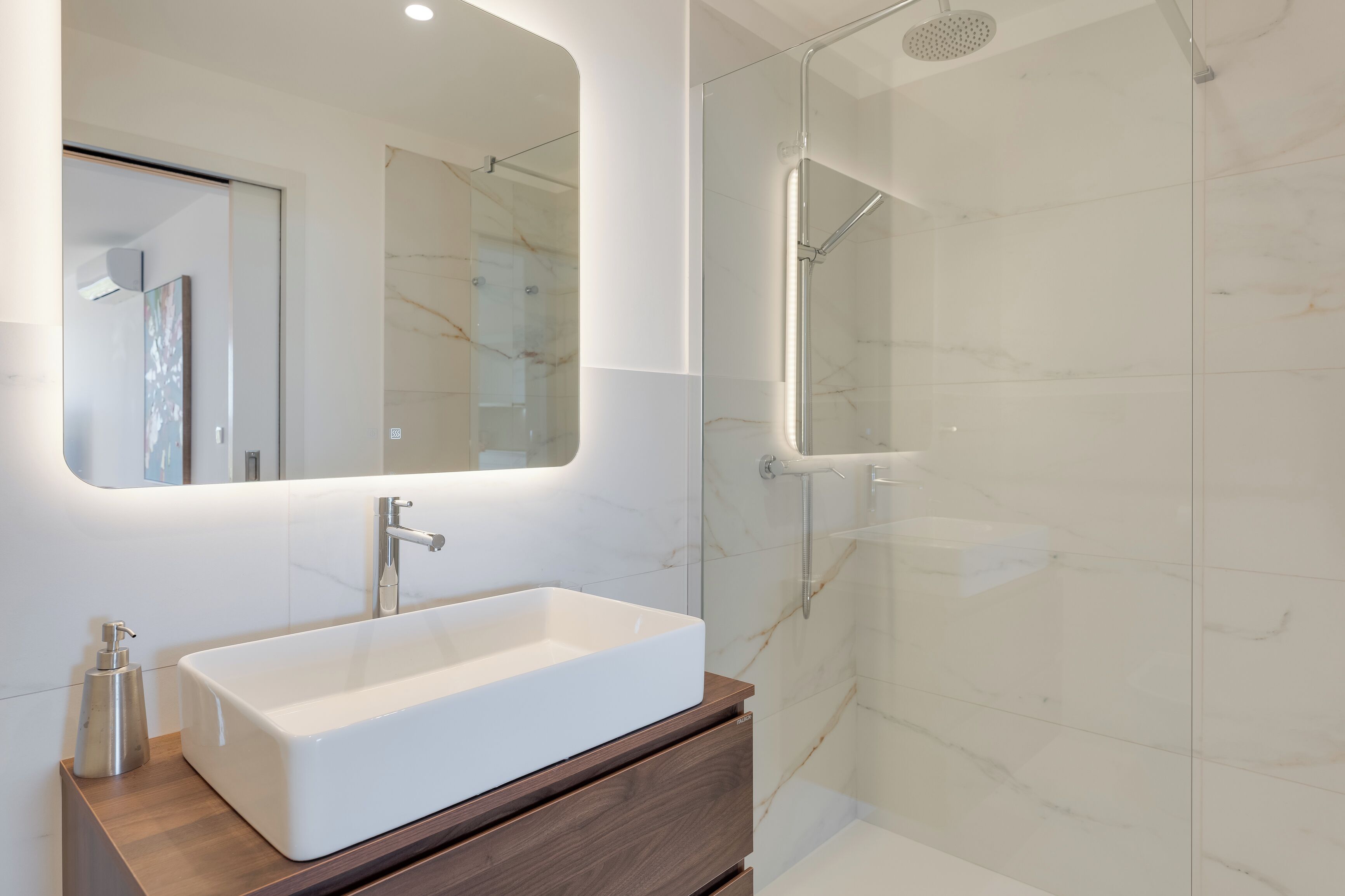Une salle de bain moderne avec un grand lavabo rectangulaire, une cabine de douche en verre et un grand miroir au-dessus du meuble-lavabo.