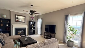 Una sala de estar con chimenea, un sofá, una mesa de centro, un televisor y un ventanal con cortinas.