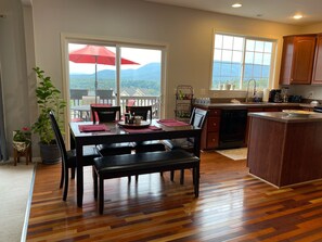 Un comedor con mesa, sillas y un paraguas rojo. Hay una zona de cocina con fregadero y armarios.