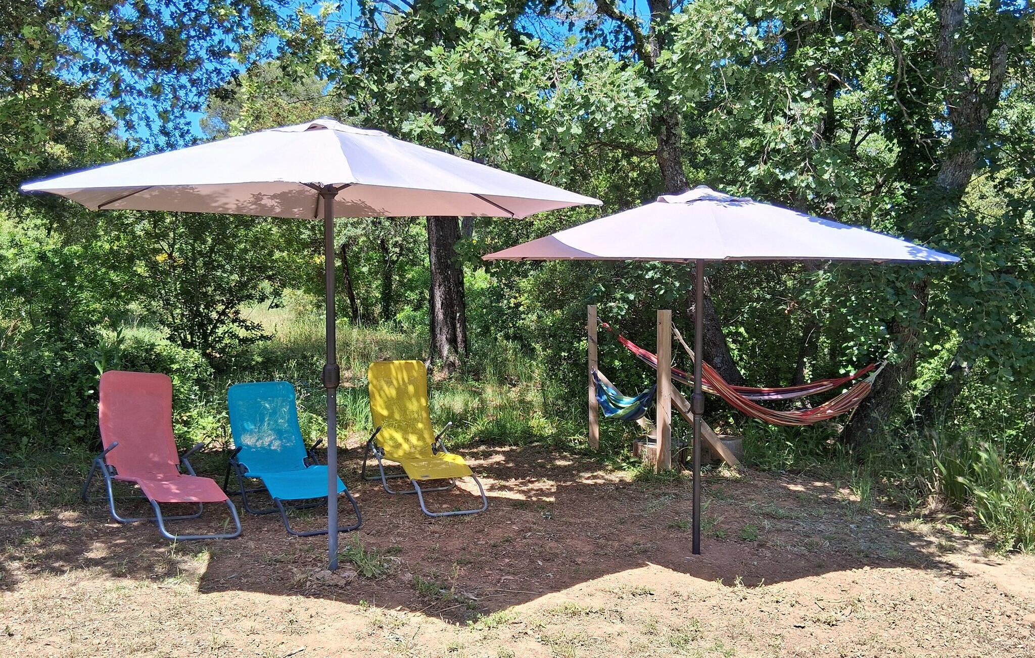 A campsite with two large umbrellas, a hammock, and three colorful chairs.
