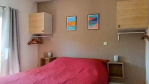 Ein Schlafzimmer mit Bett, Schrank, zwei gerahmten Bildern, einem Nachttisch und einer Pendelleuchte.