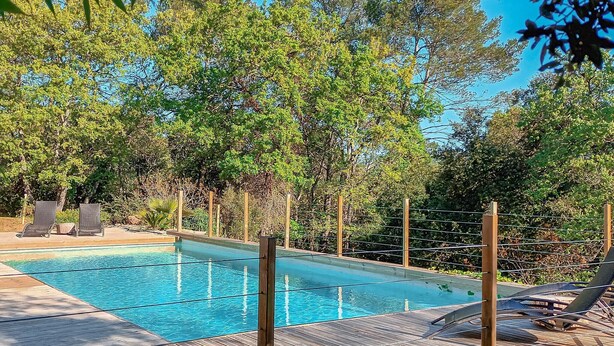 Ein Schwimmbad mit Holzterrasse, umgeben von Bäumen und einem Zaun.