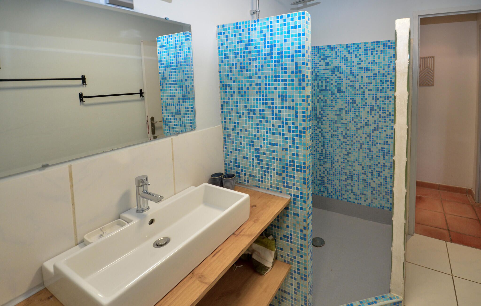 Une salle de bain avec un lavabo blanc, un miroir et une douche aux carreaux de mosaïque bleus.