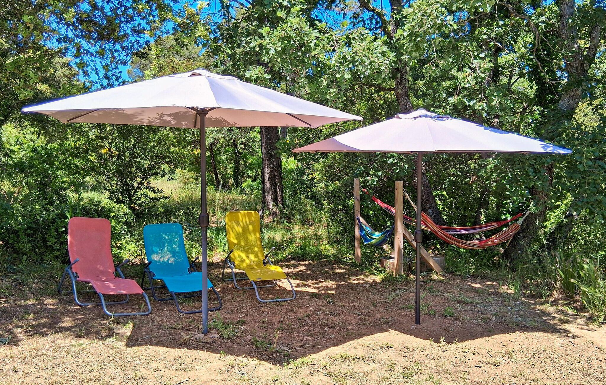 Een camping met twee grote parasols, een hangmat en kleurrijke stoelen.
