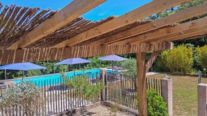 Une pergola en bois surplombant un espace piscine, agrémentée de parasols et de sièges.