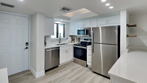 A modern kitchen with white cabinets, stainless steel appliances, and a light wood floor. - Seaside 209 (Fort Myers Beach)
