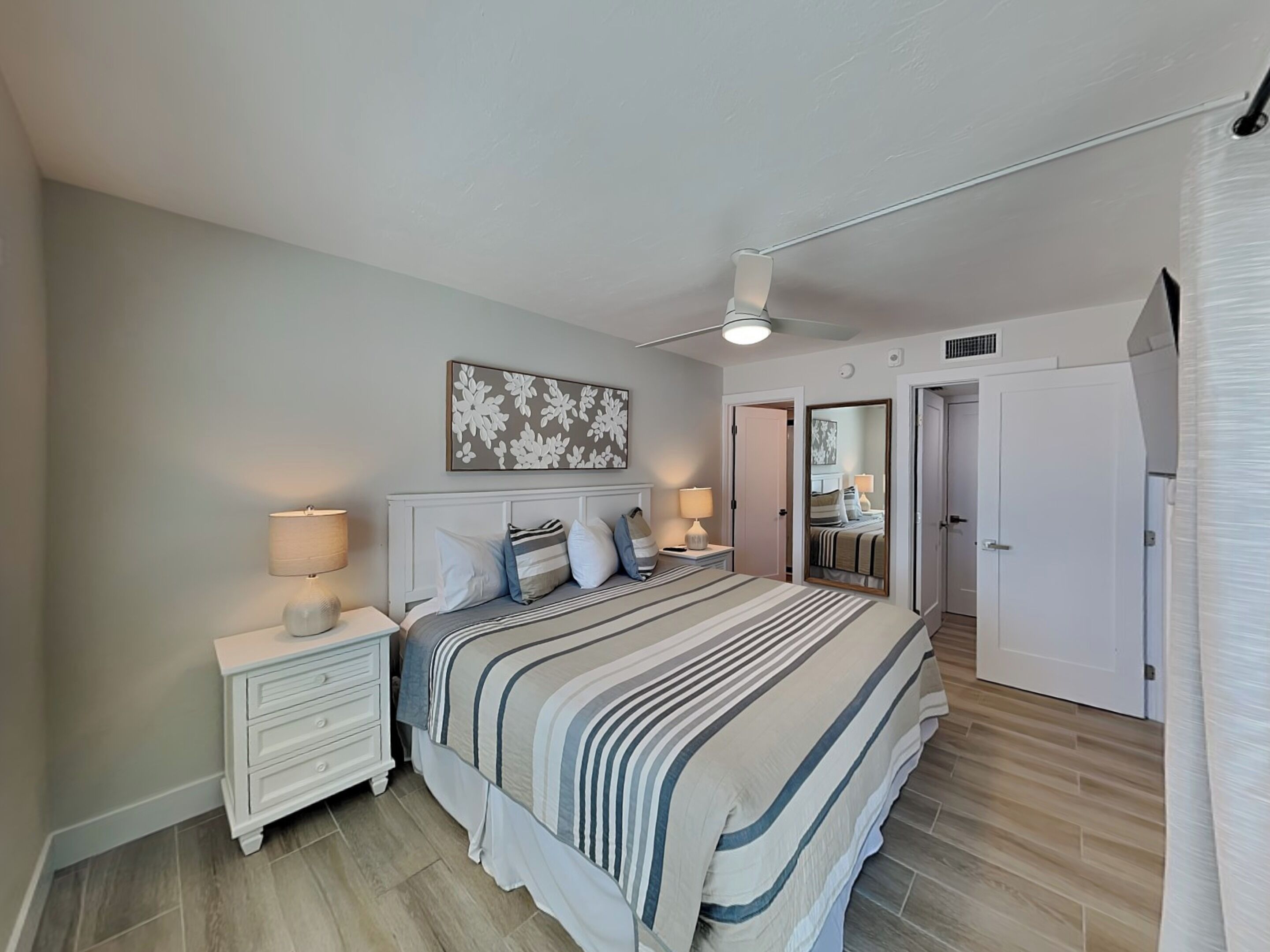 Een slaapkamer met een bed, nachtkastjes, een plafondventilator en een deur naar een andere kamer.