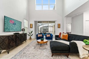 Uma sala de estar espaçosa com uma televisão grande, dois sofás, uma mesa de centro e vista para uma estufa.