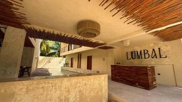 A reception area with a wooden reception desk, a wall with the word 'LUMBAL' in large letters, and a pool in the background.