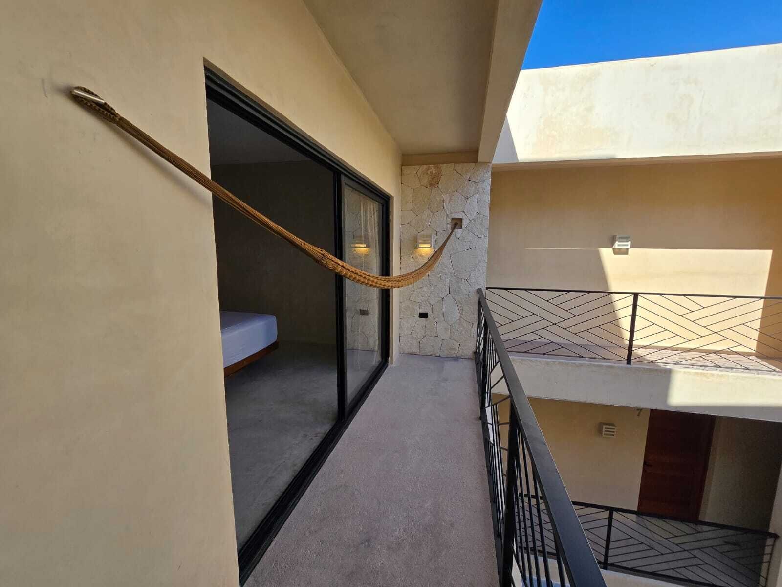 Een modern balkon met een hangmat, een glazen deur naar een slaapkamer en een stenen muur.