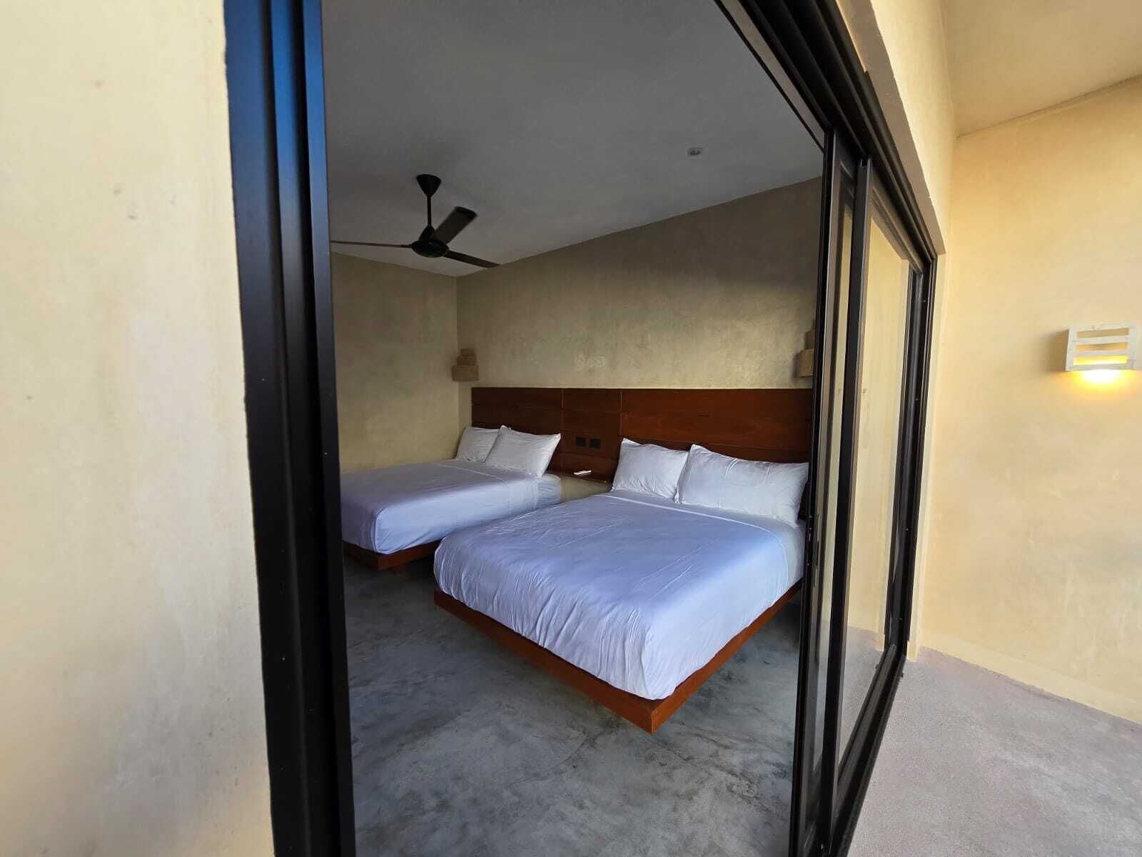 Une chambre d’hôtel avec deux lits, un ventilateur de plafond et un luminaire fixé au mur.