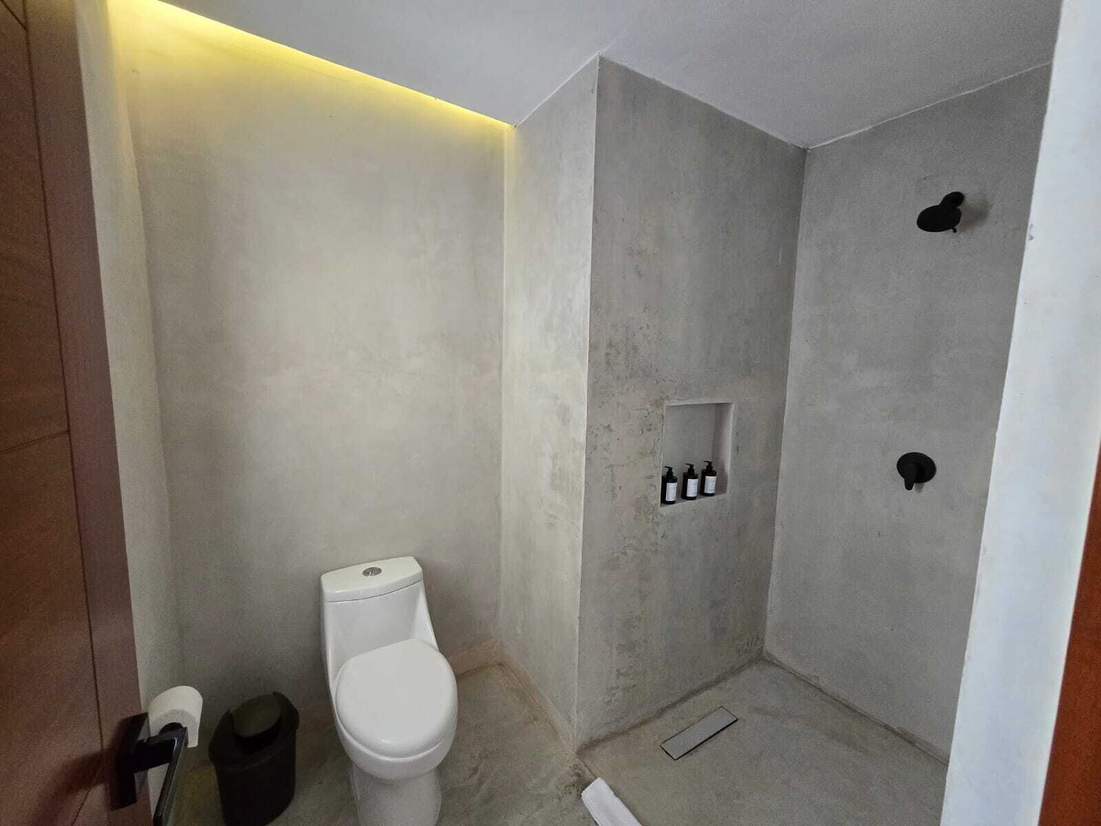 A bathroom with a toilet, a shower, and a small shelf with toiletries.