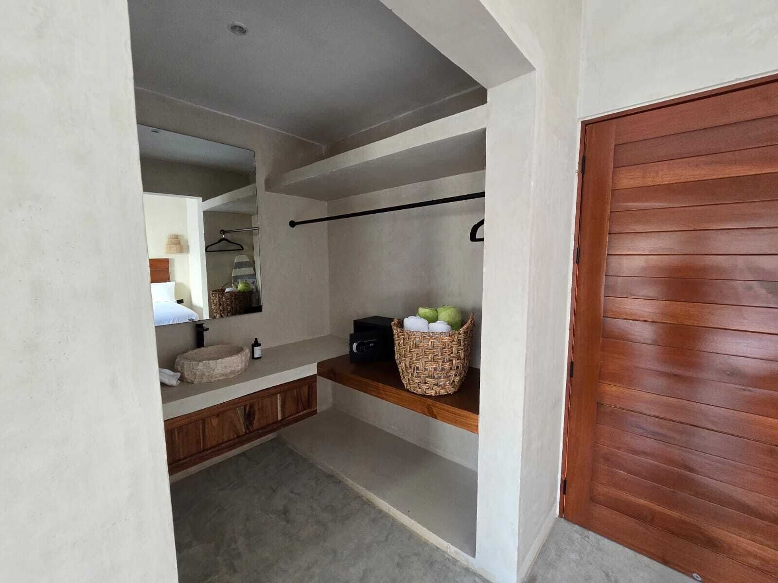 A bathroom with a wooden vanity, a mirror, a towel rack, and a basket of toiletries.