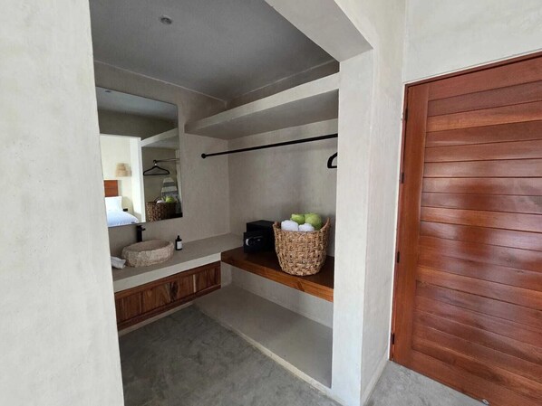 Un baño con tocador de madera, espejo, perchero y una cesta de artículos de aseo.