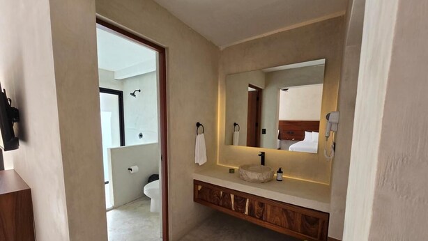 A modern bathroom with a large mirror, wooden vanity, and a wicker basket with towels. - Luumbal Hotel Boutique El Cuyo (El Cuyo)