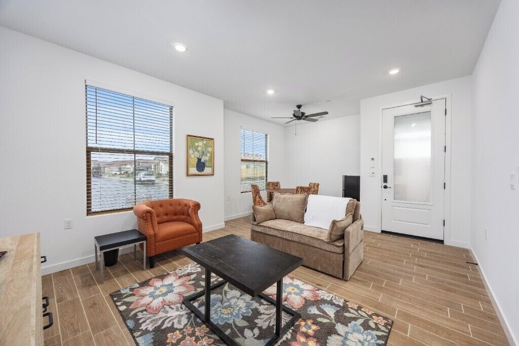 A living room with a sofa, armchair, and coffee table, a door, and windows with blinds.