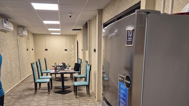 A conference room with a tiled floor, a table with chairs, and a refrigerator. - Bombay Backpackers DXB Airport (Dubai)