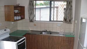 A compact kitchen with a stove, oven, sink, and wooden cabinets. - Cairns holiday unit apartment kitchen aircon wifi near esplanade and hospital (Cairns North)