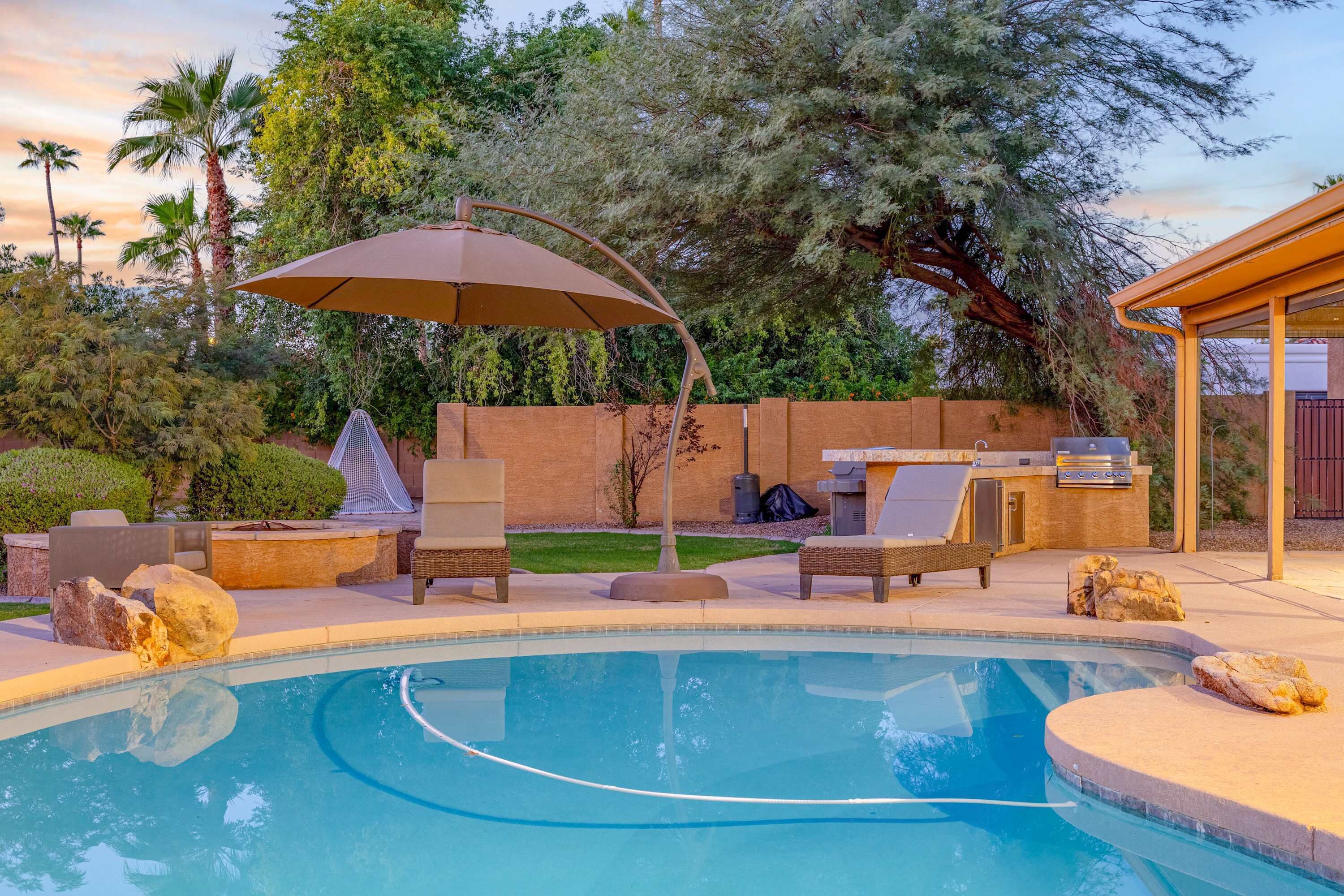 A swimming pool with lounge chairs and an umbrella, surrounded by a landscaped garden and a barbecue area.