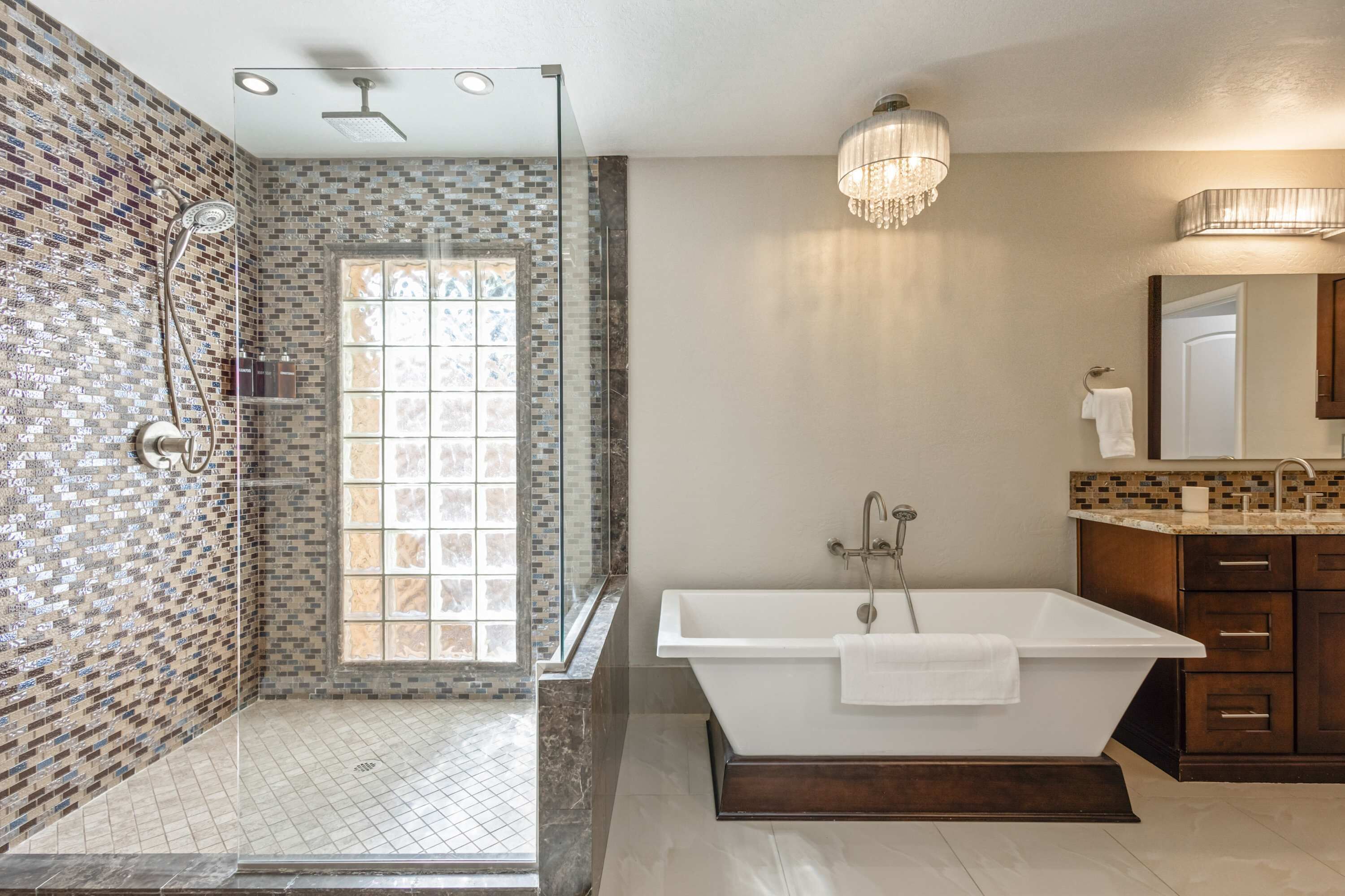 Ein modernes Badezimmer mit freistehender Badewanne, einer gläsernen Duschkabine und einem mit Mosaikfliesen ausgelegten Duschbereich.