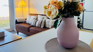 Un soggiorno con un divano, un vaso rosa con fiori e una lampada.