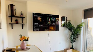Un soggiorno moderno con una TV a schermo piatto montata sulla parete, un tavolo da pranzo con sedie, una pianta in vaso e un tavolino con una scatola.