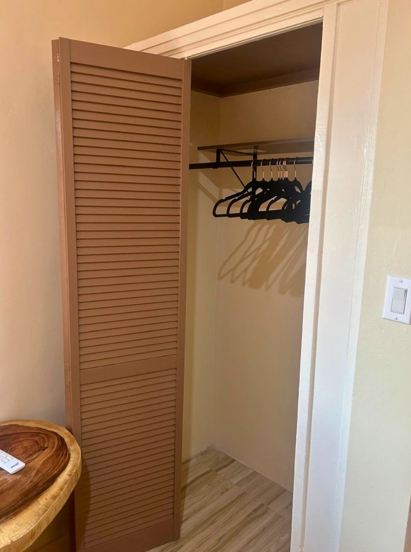 Um guarda-roupa com porta de correr, chão de madeira e cabideiro com roupas.