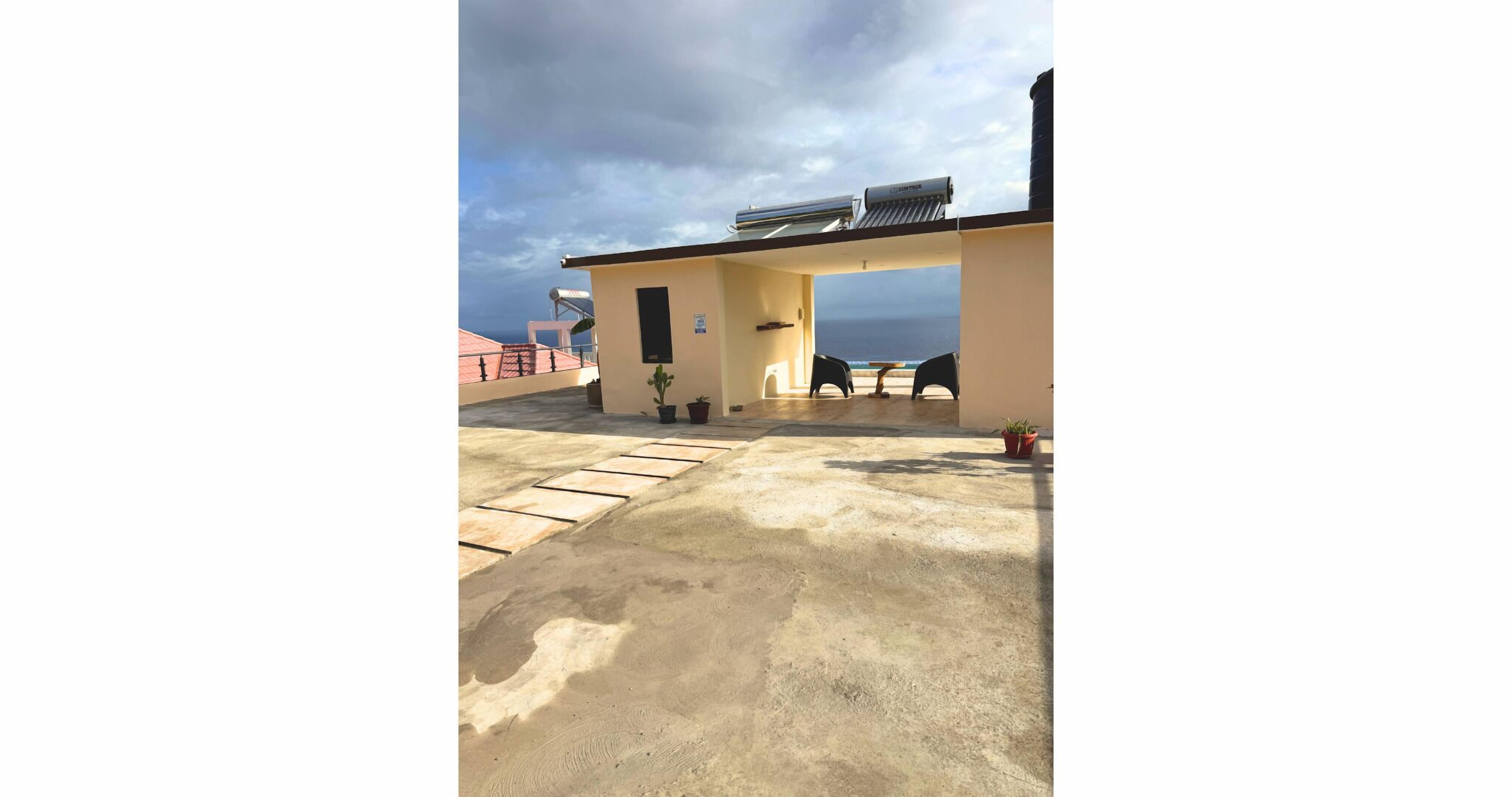 A rooftop terrace with a view of the ocean, a water heater, and potted plants.