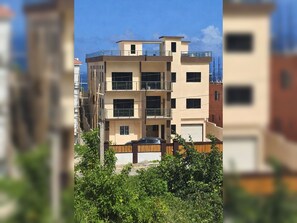 A multi-story residential building with a flat roof, balconies, and a garage. - Slow down in Tranquility Suite, a comfortable one bedroom retreat with a queen bed and ensuite bathroom. Recharge between island adventures and enjoy the villa’s shared rooftop infinity pool and bar. (Boscobel)