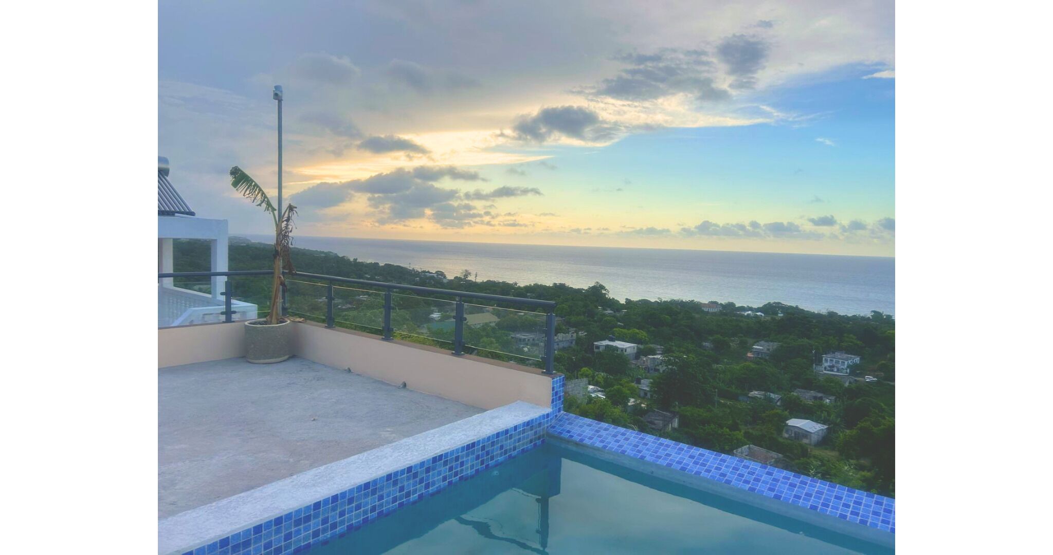 A rooftop pool with a view of the ocean and surrounding greenery.