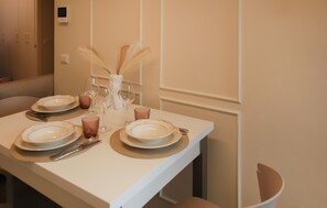 Ein Esszimmertisch ist gedeckt mit Tellern, Gläsern und Besteck, eine Vase mit Federn und eine Wandleuchte.