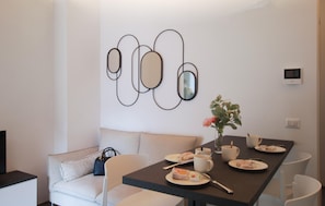 Zona pranzo con tavolo apparecchiato per due, divano e un'opera d'arte astratta appesa alla parete.