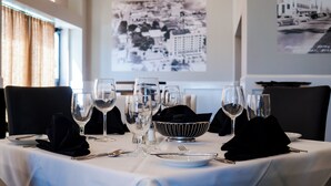 A dining table set with multiple wine glasses, a bowl, and cutlery, with a cityscape photo on the wall behind.