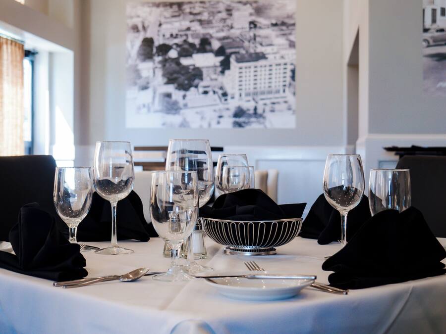 A dining table set with multiple wine glasses, a bowl, and cutlery, with a cityscape photo on the wall behind.