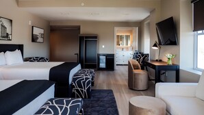 A hotel room with two beds, a desk, a chair, a small table, a mirror, and a TV.