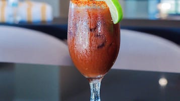 A glass of a red beverage with a lime garnish on a table in a room with a blurred background.