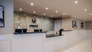 A hotel reception desk with a marble wall, a logo, and a door in the background.