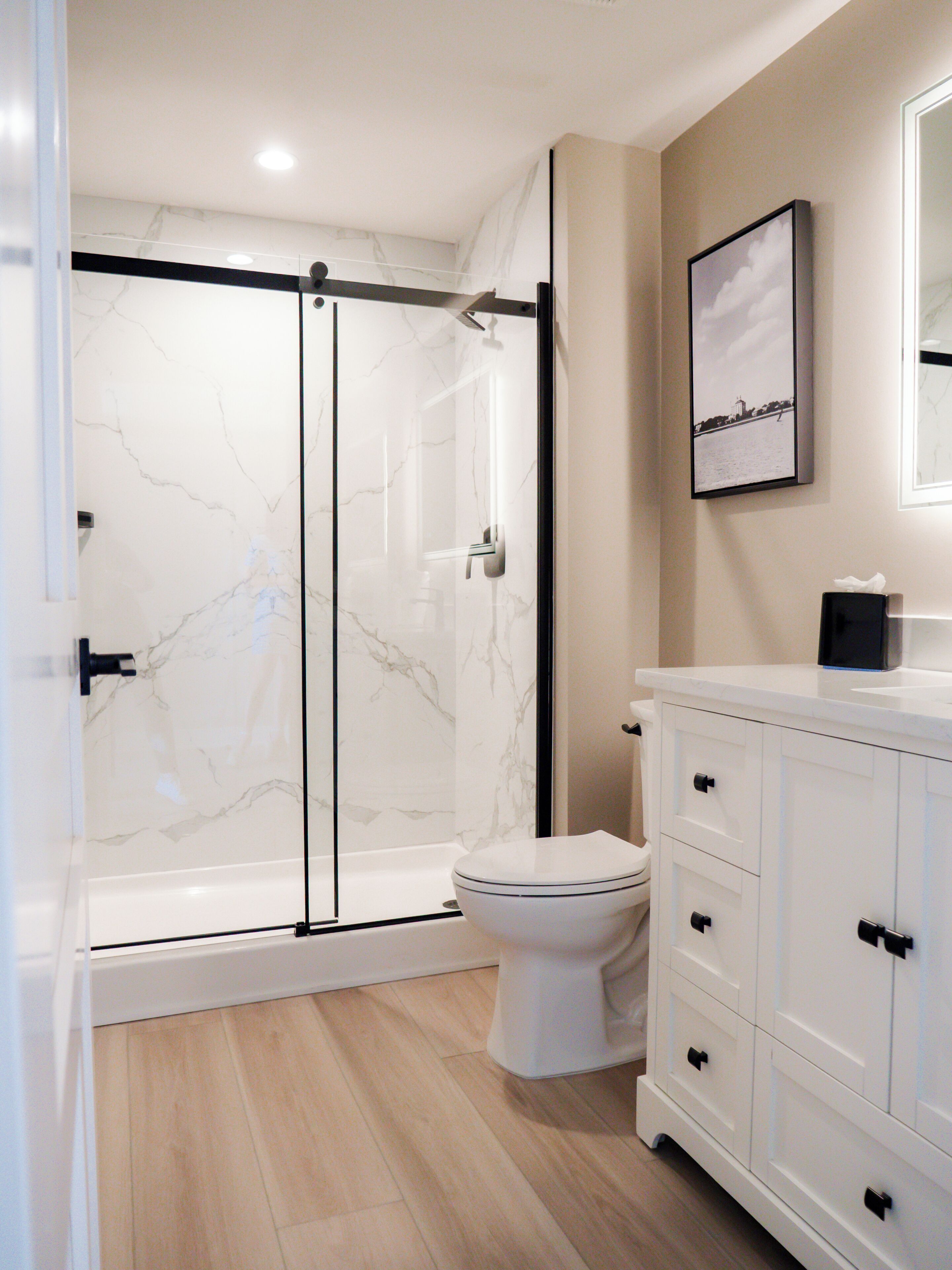 A bathroom with a glass-enclosed shower, a toilet, and a vanity with drawers.