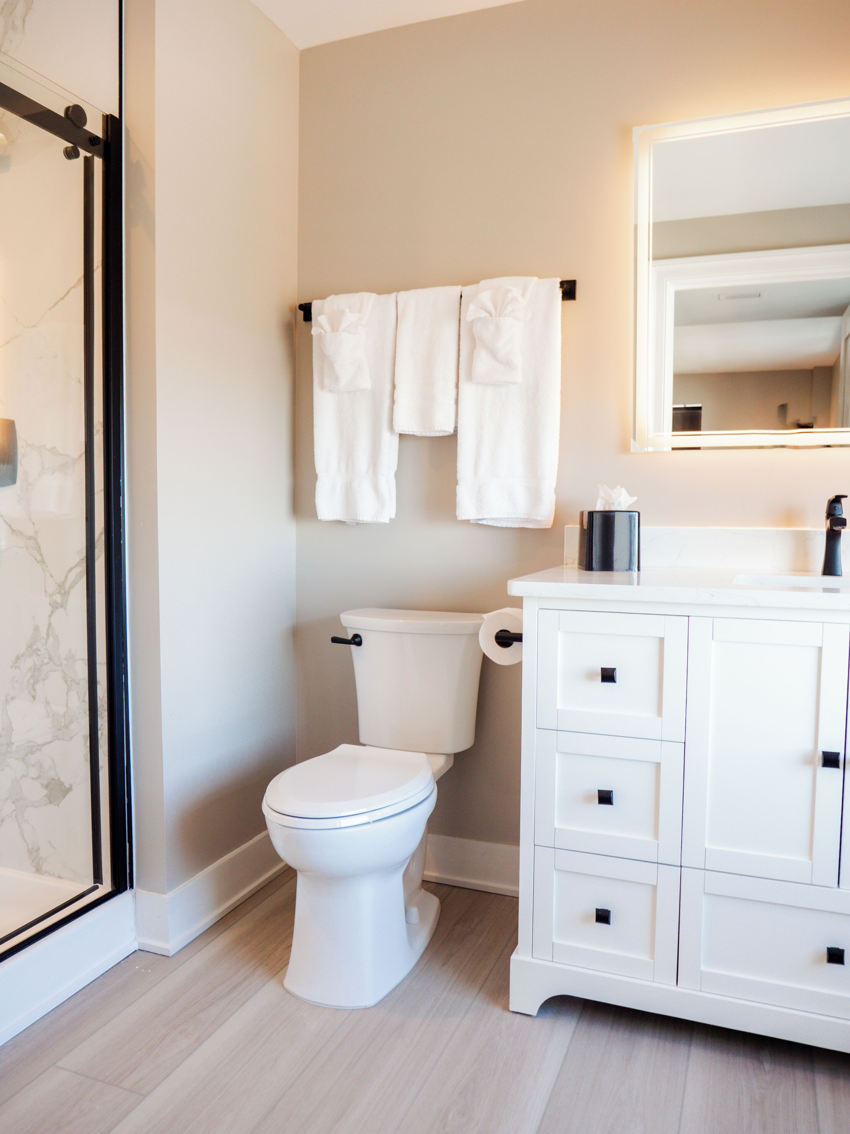 Une salle de bain avec des toilettes, un meuble blanc avec des tiroirs, un porte-serviettes avec des serviettes et un miroir au-dessus du lavabo.