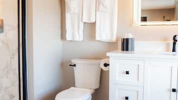 Une salle de bain avec des toilettes, un meuble blanc avec des tiroirs, un porte-serviettes avec des serviettes et un miroir au-dessus du lavabo.