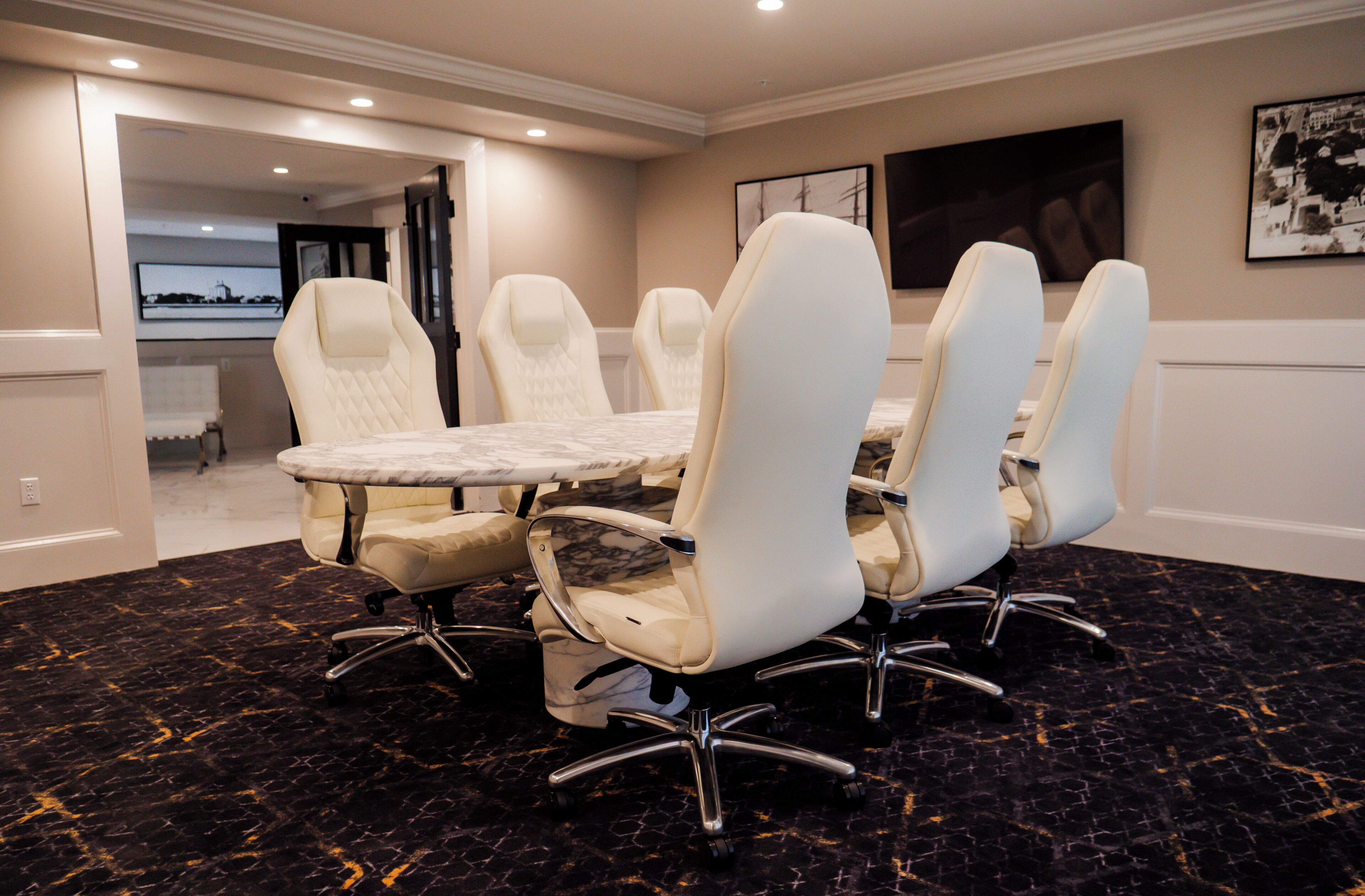A conference room with a marble table and white chairs, carpeted floor, and artwork on the walls.