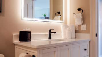 Um banheiro com toucador branco, espelho com iluminação embutida, porta-toalhas e vaso sanitário.