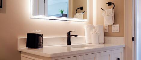 Un baño con tocador blanco, espejo con iluminación integrada, toallero y un inodoro.